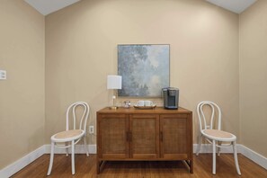 Una habitación con un armario de madera, dos sillas blancas, una cafetera y una lámpara de pared.