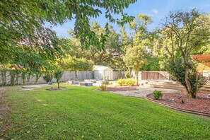 Un patio trasero con césped, un árbol, un cobertizo y una valla de madera.