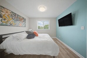 A bedroom with a bed, a flat-screen TV, a window, and a ceiling light.
