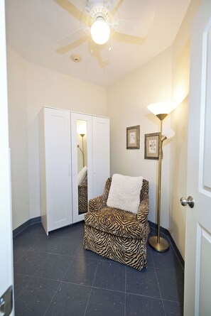 Een kamer met een stoel met zebraprint, een witte garderobe, een vloerlamp en ingelijste foto's aan de muur.