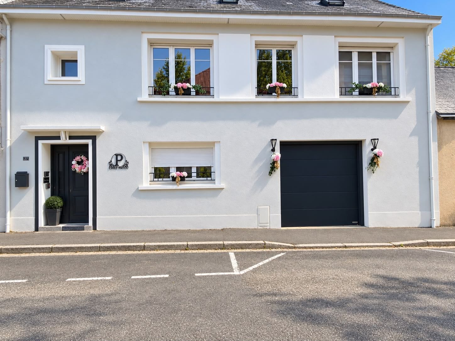A two-story building with a black front door, a garage door, and multiple windows with flower boxes.