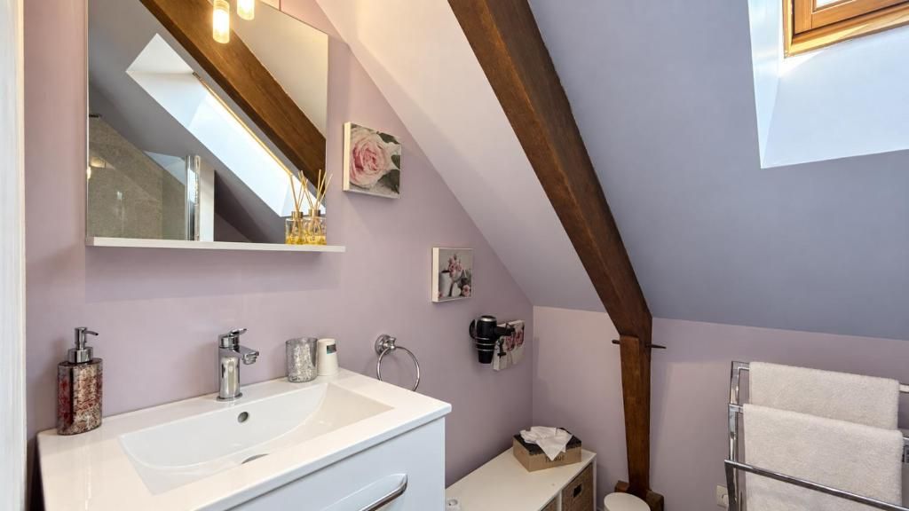 A bathroom with a large mirror, a white sink, a towel rack, and a wooden ceiling beam.