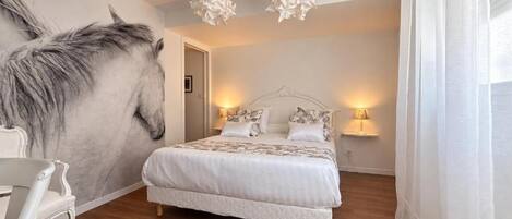 Un dormitori amb un mural gran de cavalls, un llit amb roba de llit blanca, dues làmpades de nit i un paviment de fusta.