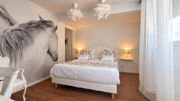 Un dormitorio con un gran mural de caballos, una cama con ropa blanca, dos lámparas de noche y piso de madera.