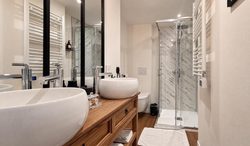 A modern bathroom with two sinks, a glass shower enclosure, and a wooden vanity.
