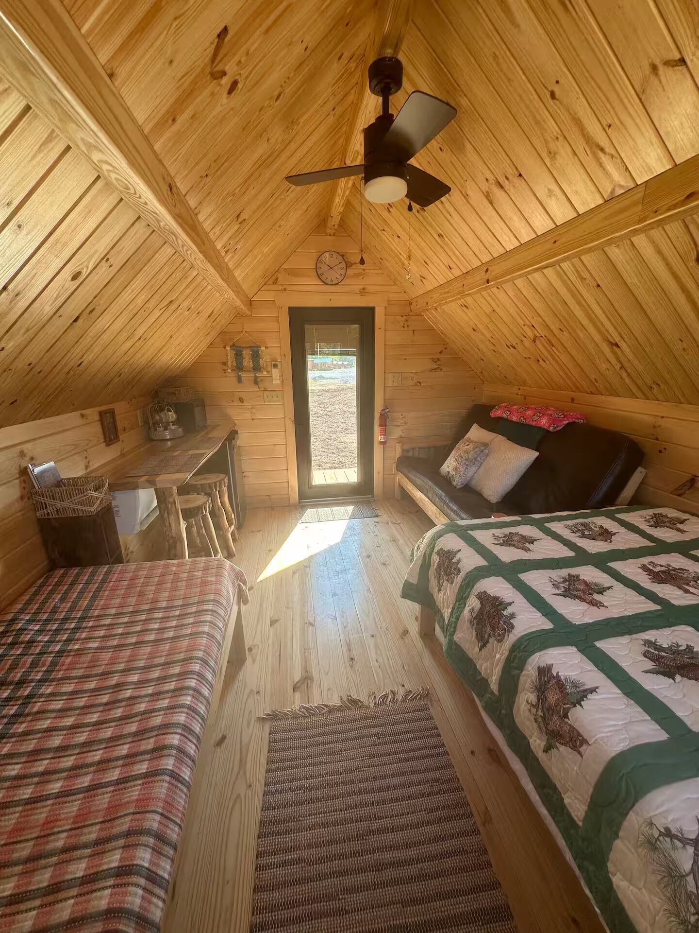 Un dormitorio acogedor en el ático, con techo inclinado, cama, sofá y una pequeña mesa con una silla.