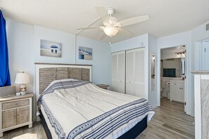 Ein Schlafzimmer mit Bett, Nachttisch, Lampe, Deckenventilator, Kleiderschrank und einem durchgegangenen Tür sichtbaren Badezimmer.