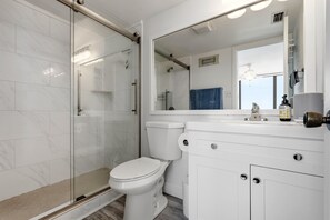 Ein modernes Badezimmer mit Duschkabine aus Glas, einer weißen Toilette und einem Waschtisch mit Spiegel.