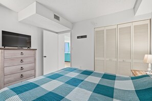 A bedroom with a checkered bedspread, a television on a dresser, and a wardrobe with louvered doors. - Oceanfront Condo with Balcony and Beach Views — Shore Drive, Myrtle Beach (Myrtle Beach)