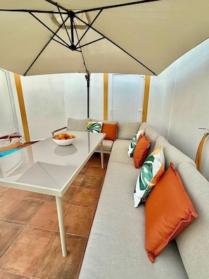 Área externa com espaço de estar, incluindo mesa, cadeiras e um sofá sob uma estrutura em forma de tenda.