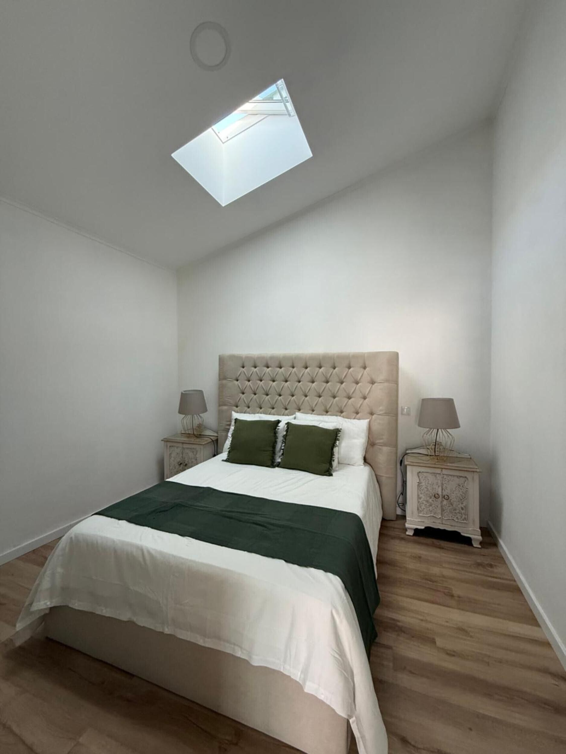 Un dormitorio con una cama, un tragaluz, dos mesitas de noche y una mesilla.