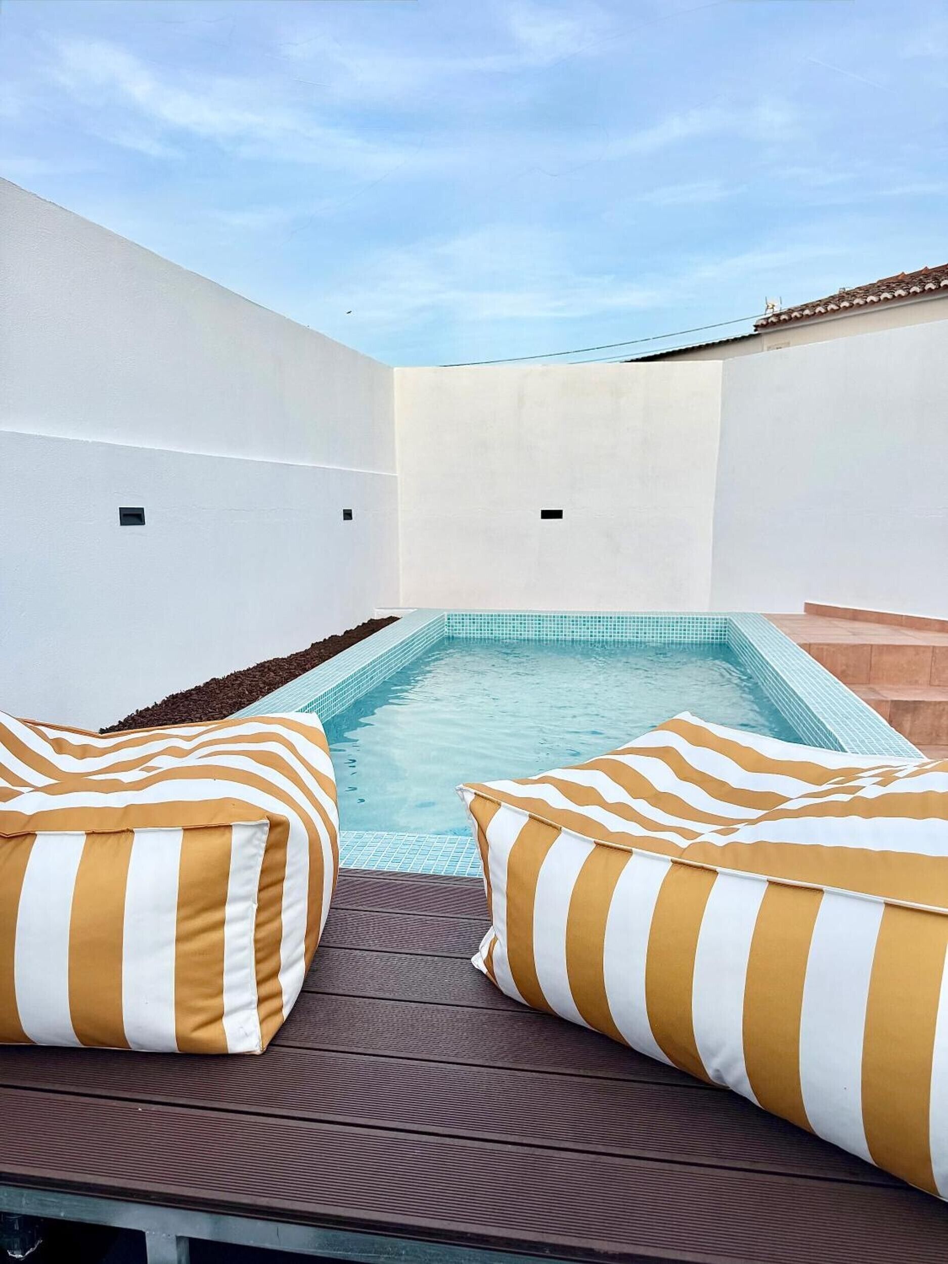Un área de piscina en la azotea con dos cojines a rayas y un cielo azul despejado.