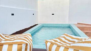 Un área de piscina en la azotea con dos cojines a rayas y un cielo azul despejado.