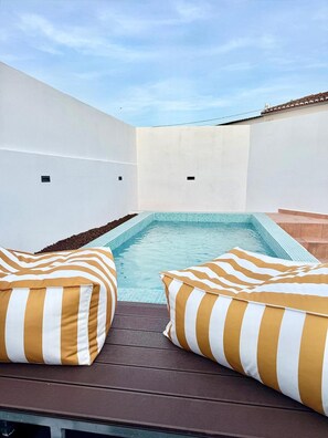 Uma área de piscina no terraço, com dois apoios de cabeça listrados e um céu azul límpido.