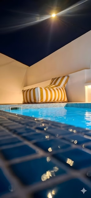 Une piscine avec un bord carrelé, un jacuzzi au premier plan et un coussin rayé adossé au mur.