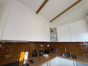 Une cuisine moderne avec des armoires blanches, un mur de fond en briques et une poutre en bois au plafond.