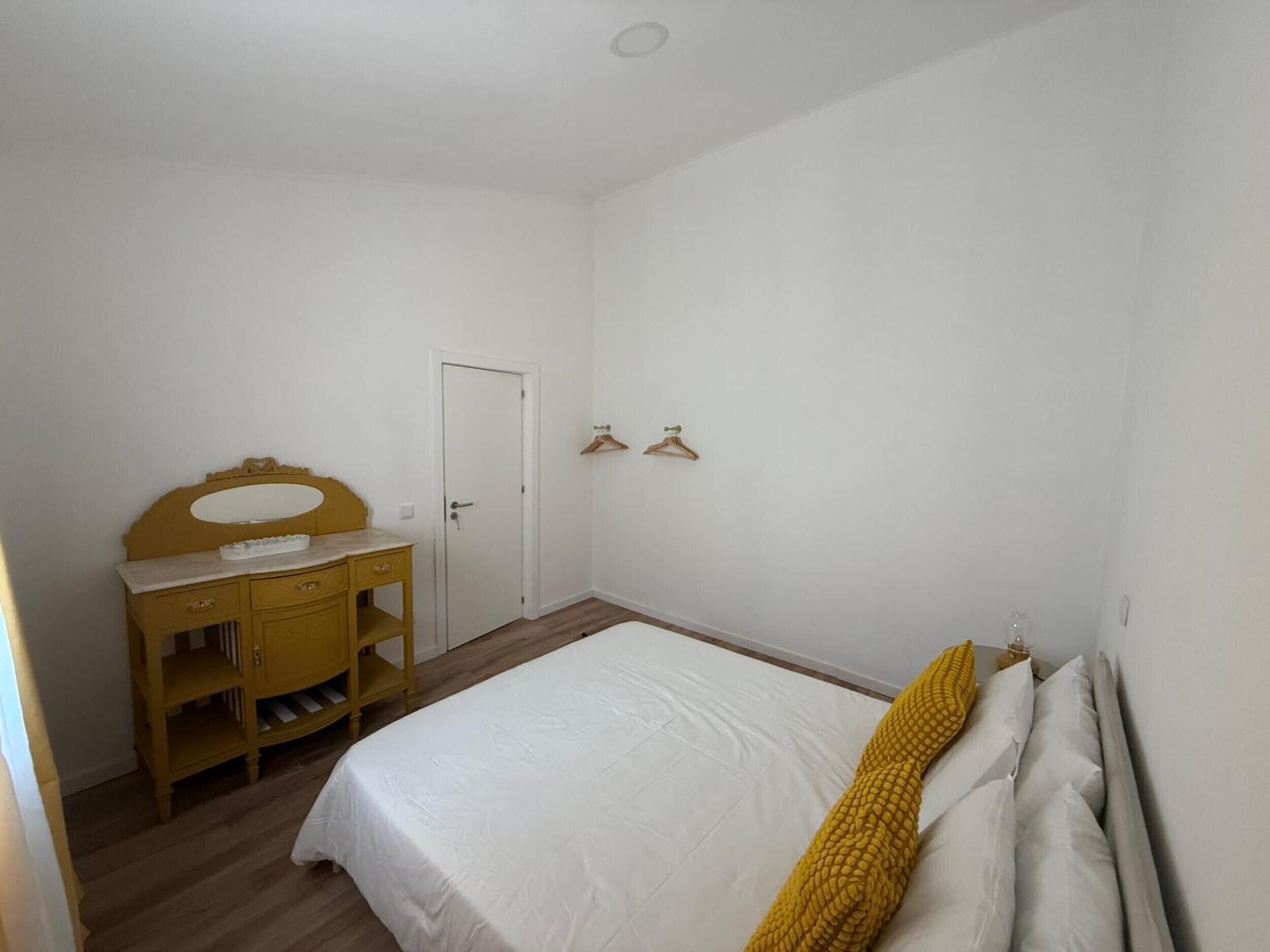 A bedroom with a bed, a dresser, a door, and a wall-mounted light fixture.