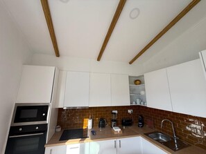 Una cocina con armarios blancos, horno empotrado, microondas, cafetera y un lavabo.