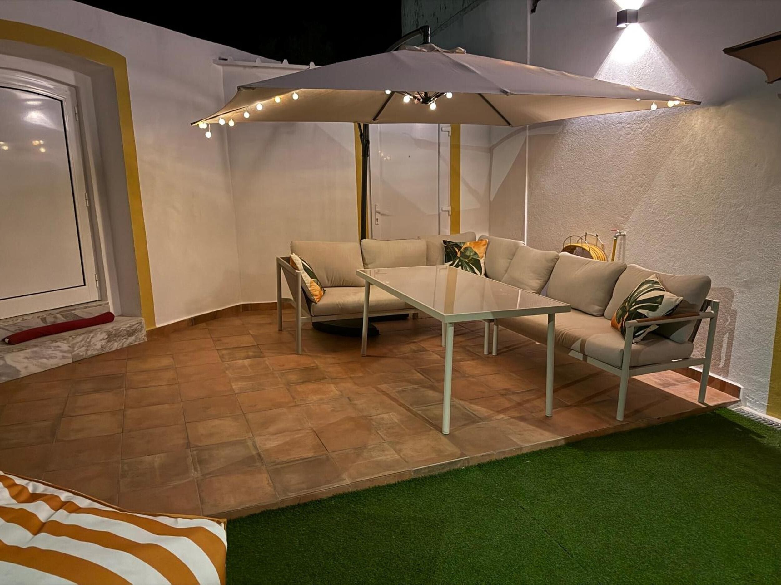 A patio area with a table and two sofas, an umbrella, and artificial grass.