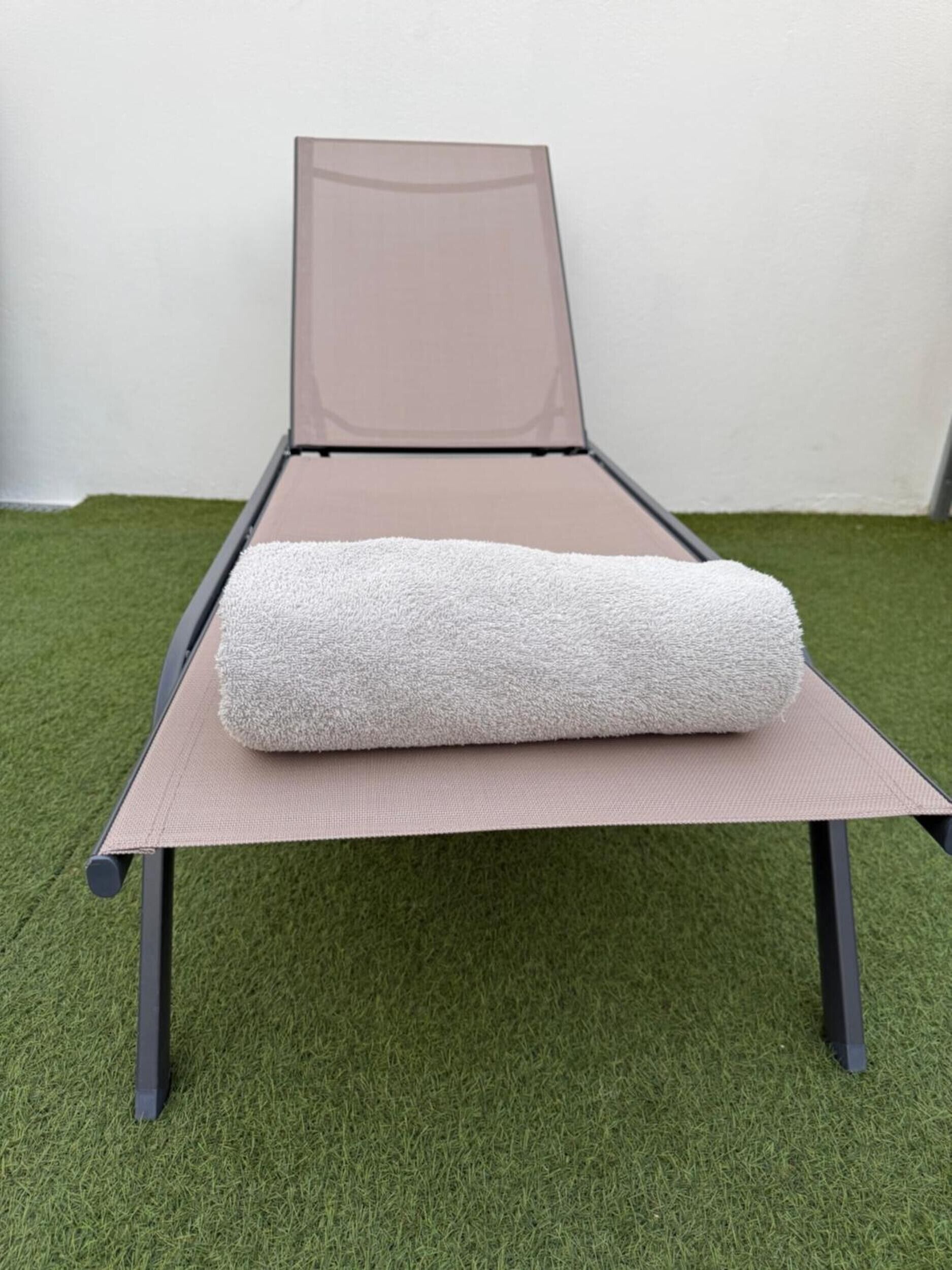A single bed with a mattress and a rolled-up blanket on a platform with a mesh headboard. The bed is placed on a green artificial grass floor.