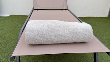 A single bed with a mattress and a rolled-up blanket on a platform with a mesh headboard. The bed is placed on a green artificial grass floor.
