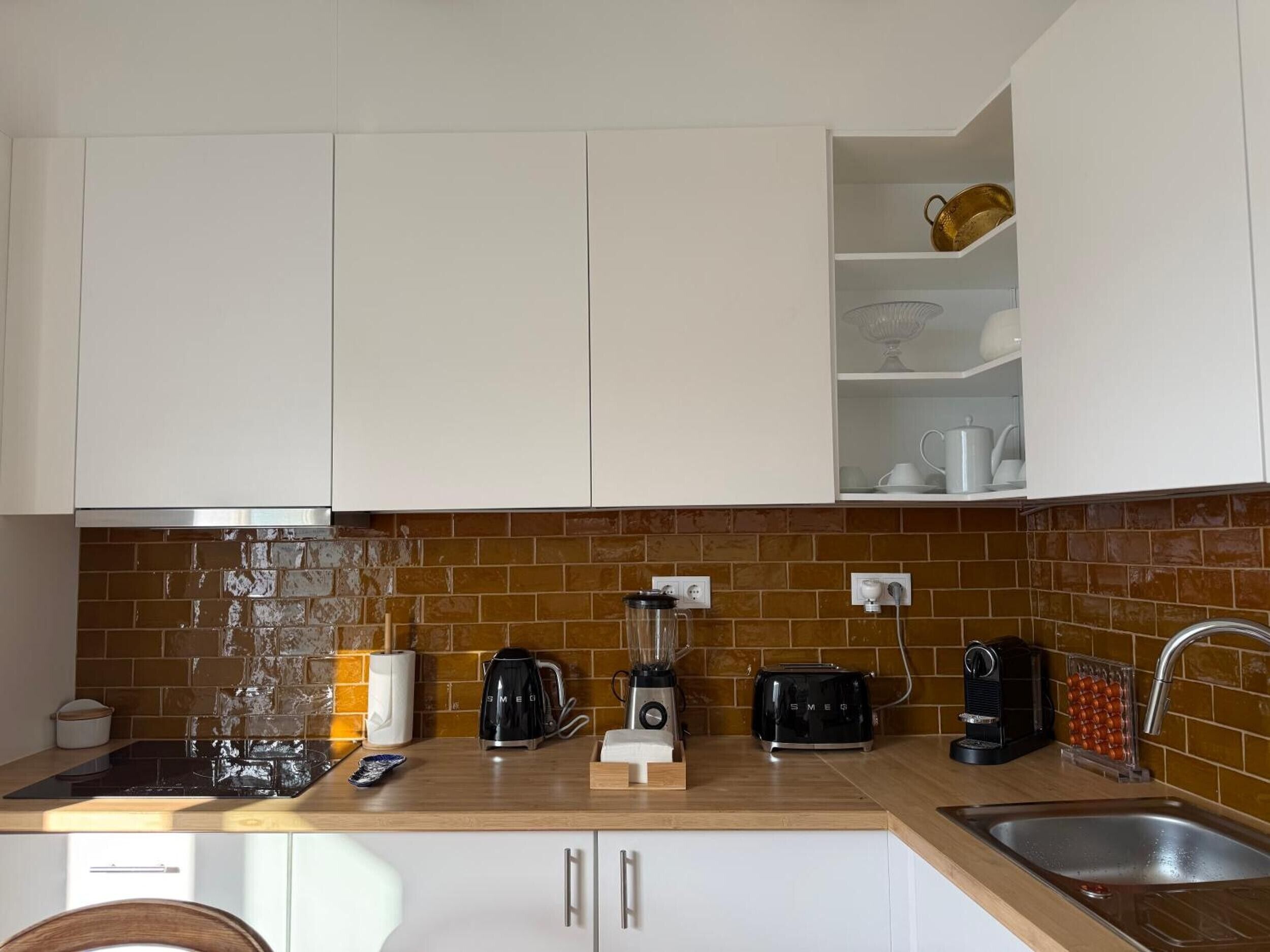 A kitchen with white cabinets, a brick backsplash, and various appliances including a coffee maker, toaster, and blender.