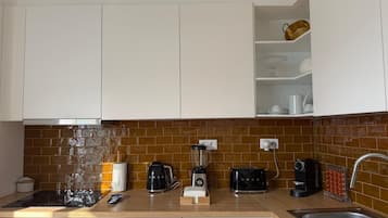 A kitchen with white cabinets, a brick backsplash, and various appliances including a coffee maker, toaster, and blender.