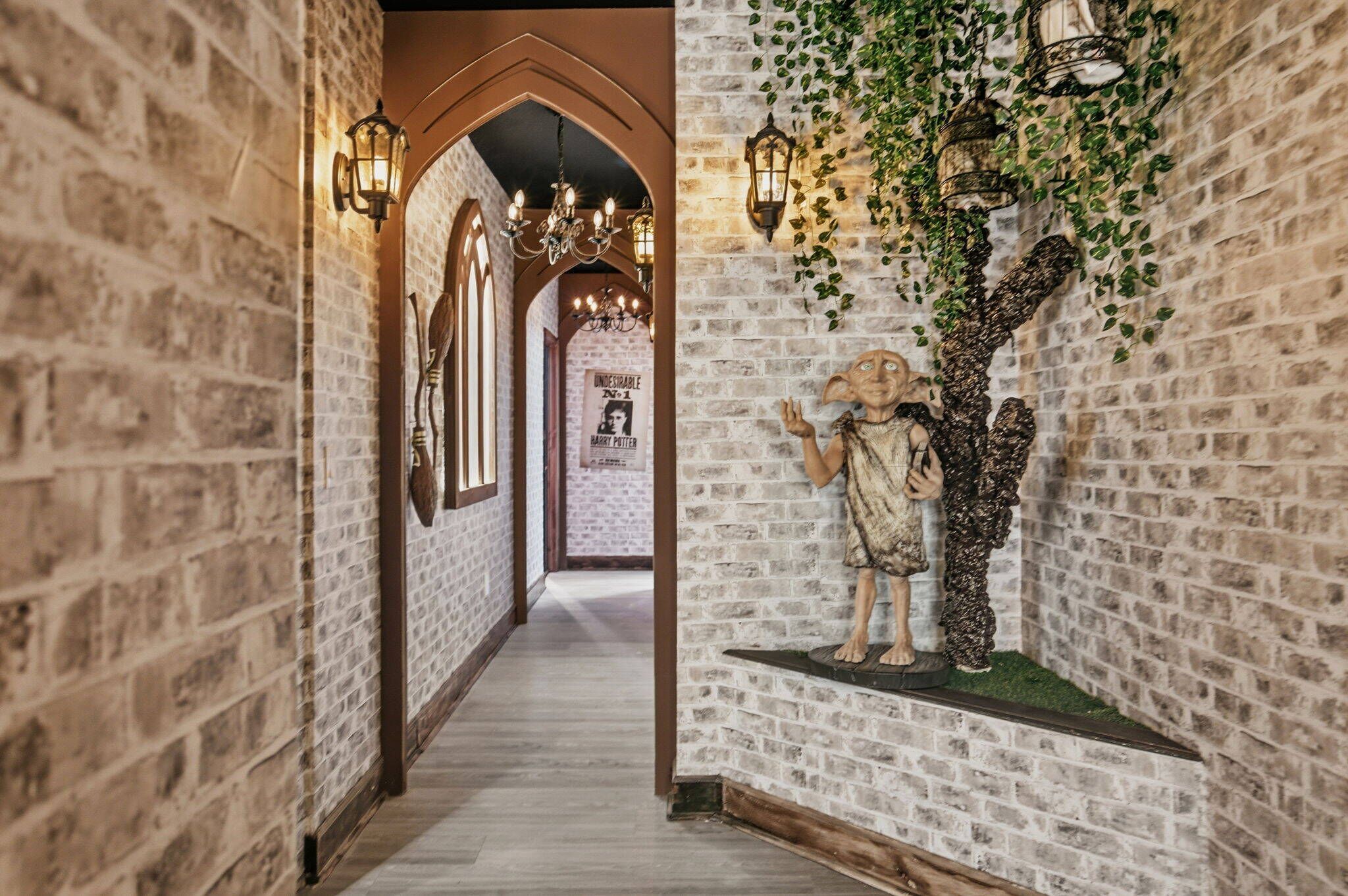 A hallway with brick walls, a wooden floor, and a statue of a character. There are wall sconces and a poster visible.