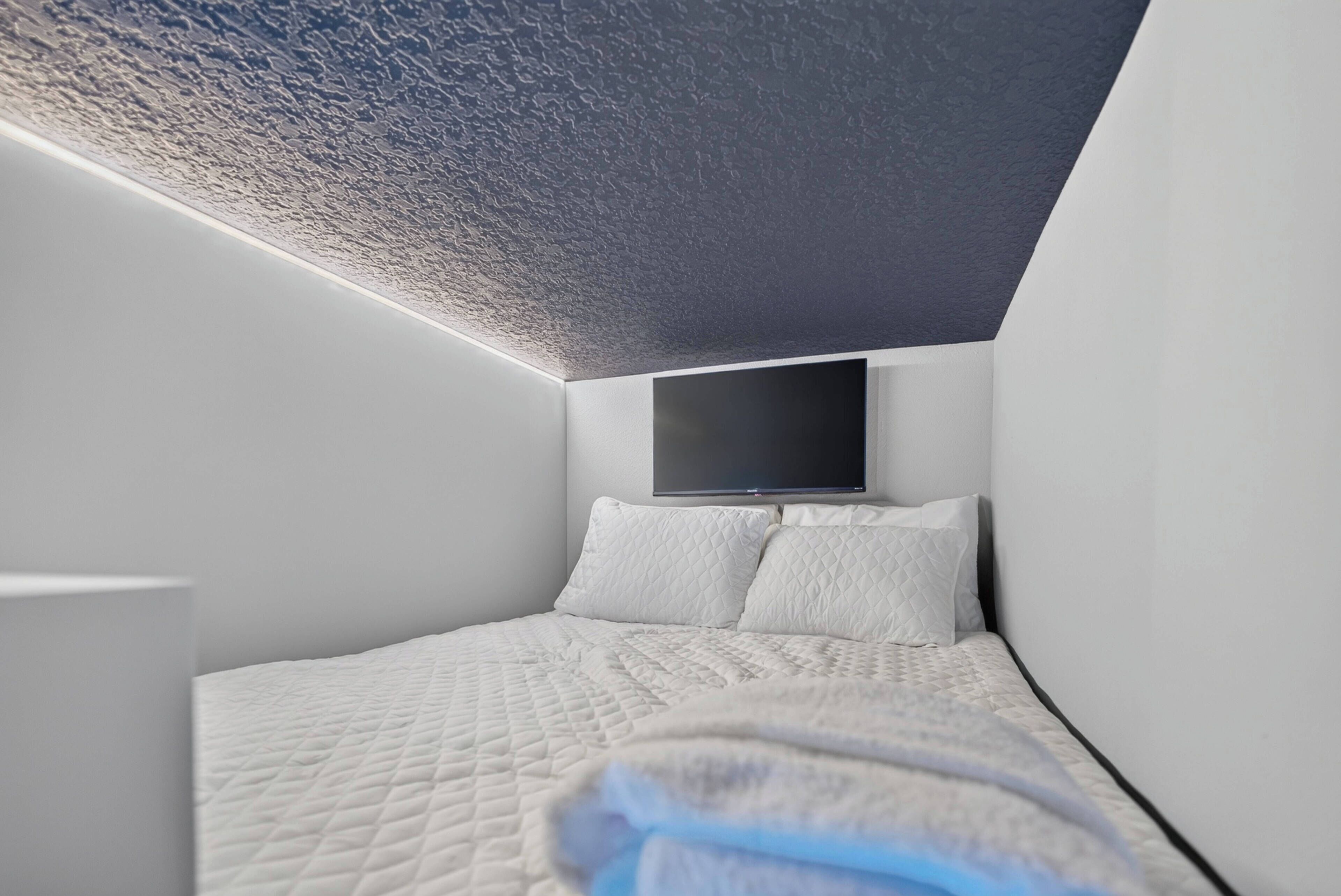 A modern bedroom with a bed, pillows, and a flat-screen TV mounted on the wall.