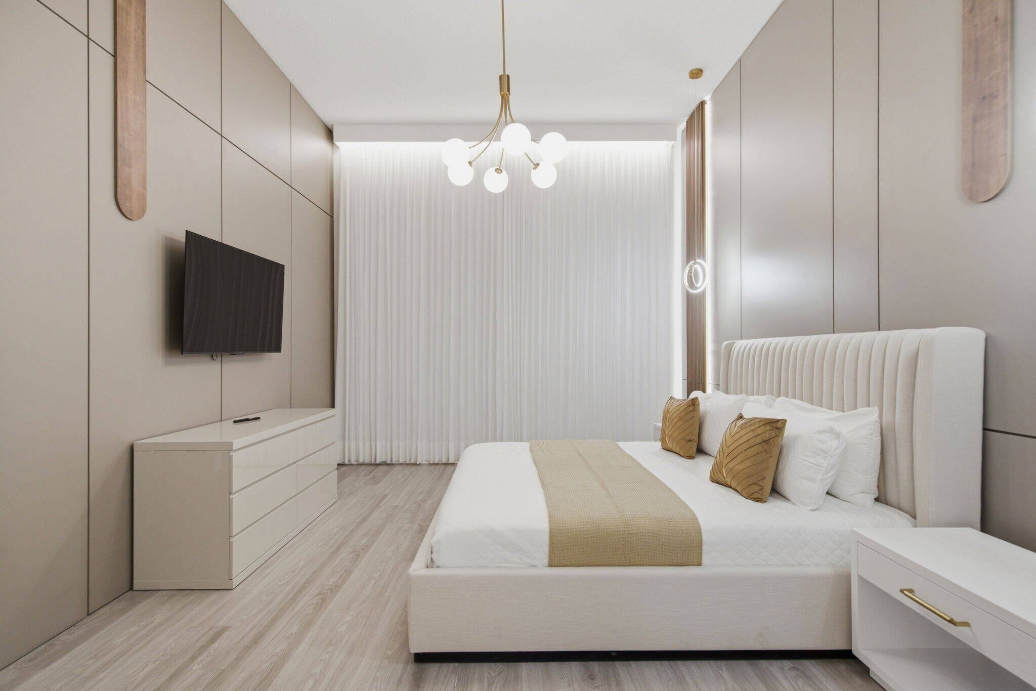 A modern bedroom with a bed, bedside tables, a TV, and a unique chandelier.