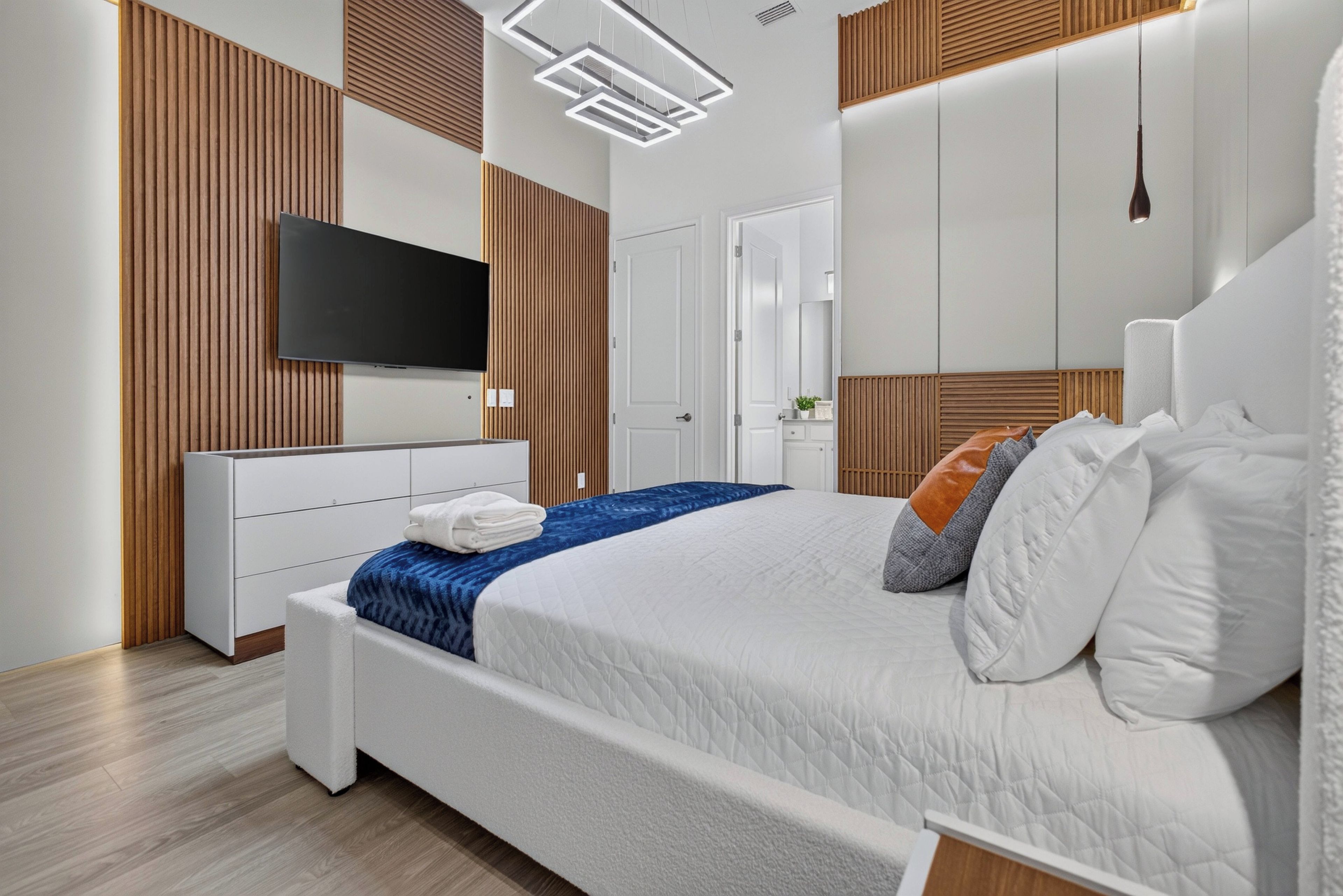 A modern bedroom with a large bed, a flat-screen TV, and a wooden headboard.
