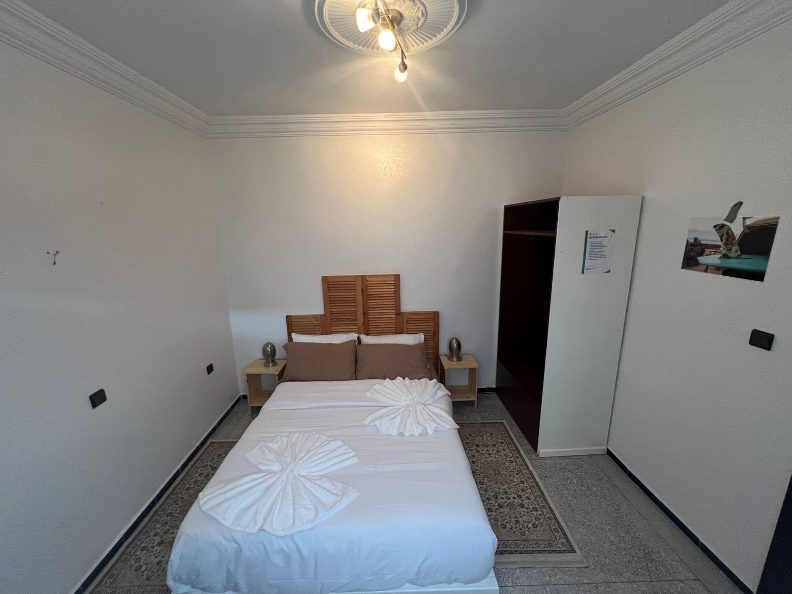 Quarto de hotel com cama, mesas de cabeceira, guarda-roupa e ventoinha no teto.