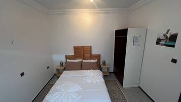 Quarto de hotel com cama, mesas de cabeceira, guarda-roupa e ventoinha no teto.