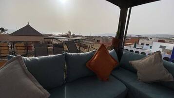 Área de estar no terraço com sofá e almofadas, com vista para a cidade.