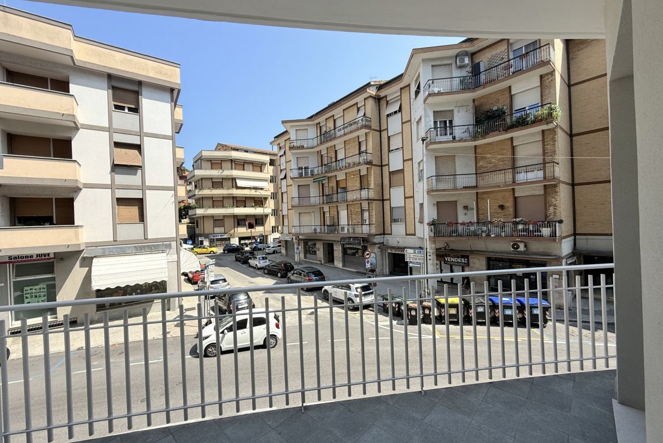 A multi-story residential building with balconies, a street view, and parked cars.