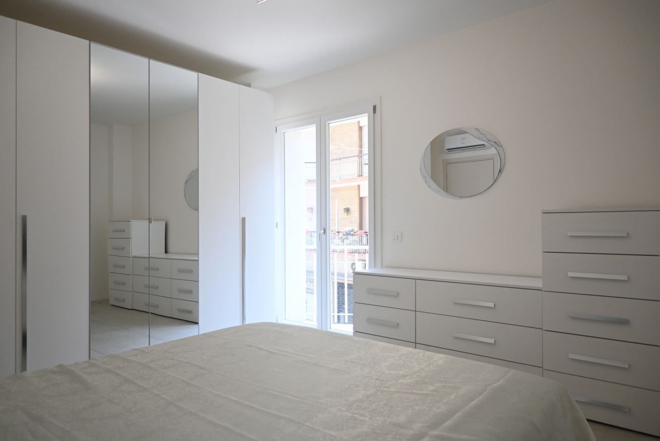 A bedroom with a bed, a wardrobe, a mirror, and a sliding door to a balcony.