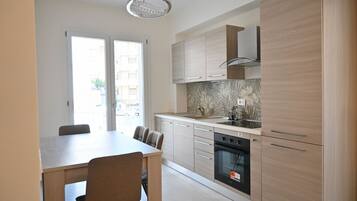 A modern kitchen with a dining area, featuring light wood cabinetry, a built-in oven, and a large window.