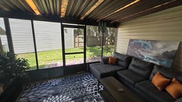 Ein modernes Wohnzimmer mit einer Eckcouch, einem gemusterten Teppich und einem großen Fenster mit Blick auf den Garten.