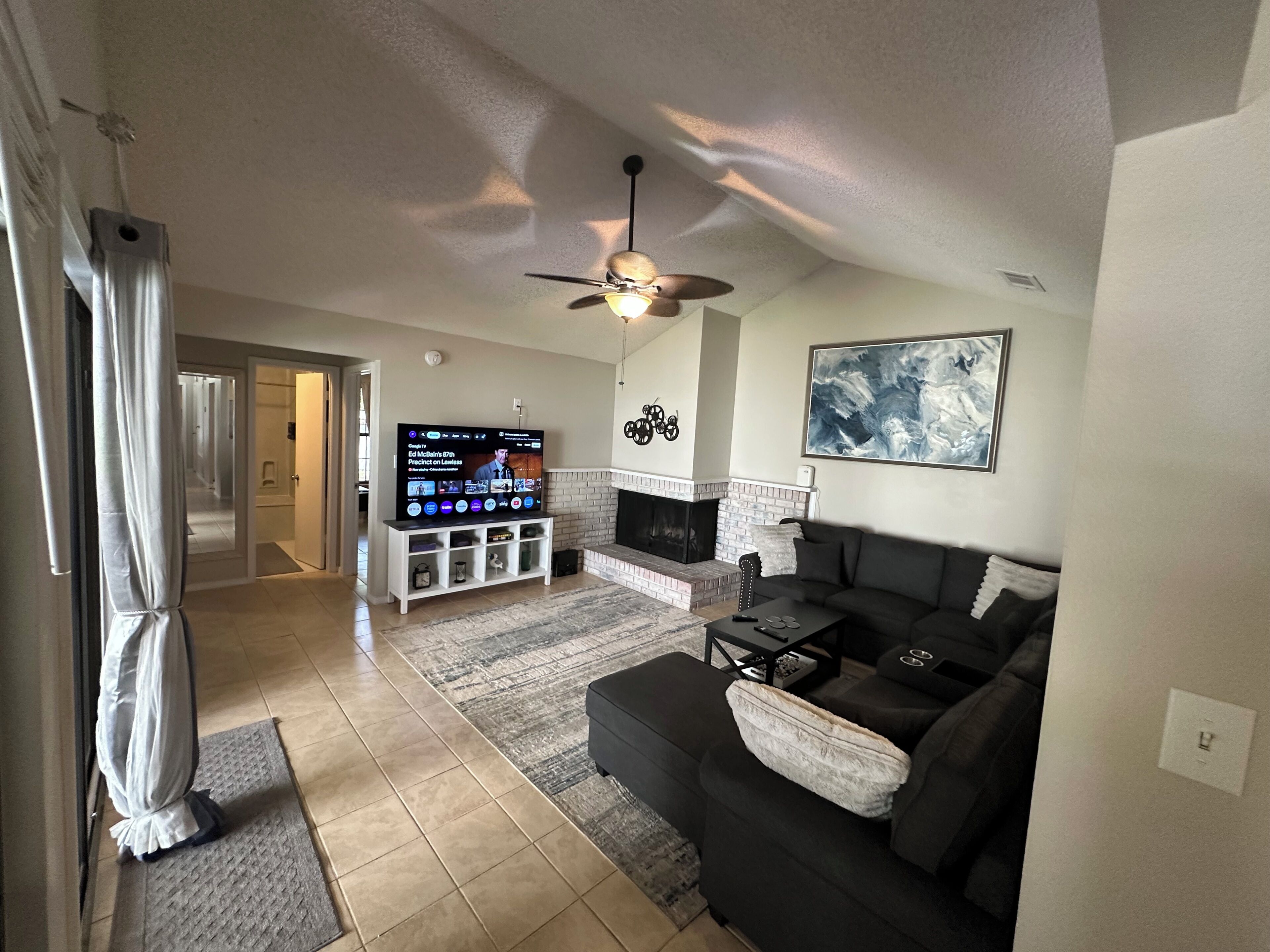 Ein Wohnzimmer mit Fernseher, einer Couch, Kamin und Deckenventilator.