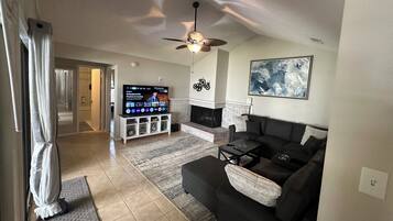 Ein Wohnzimmer mit Fernseher, einer Couch, Kamin und Deckenventilator.