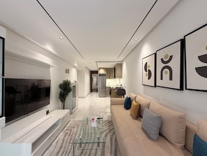 A modern living room with a flat-screen TV, a glass coffee table, a beige sofa with cushions, and framed artwork on the wall. - Golden Maarif Palmiers Apartment (Casablanca)