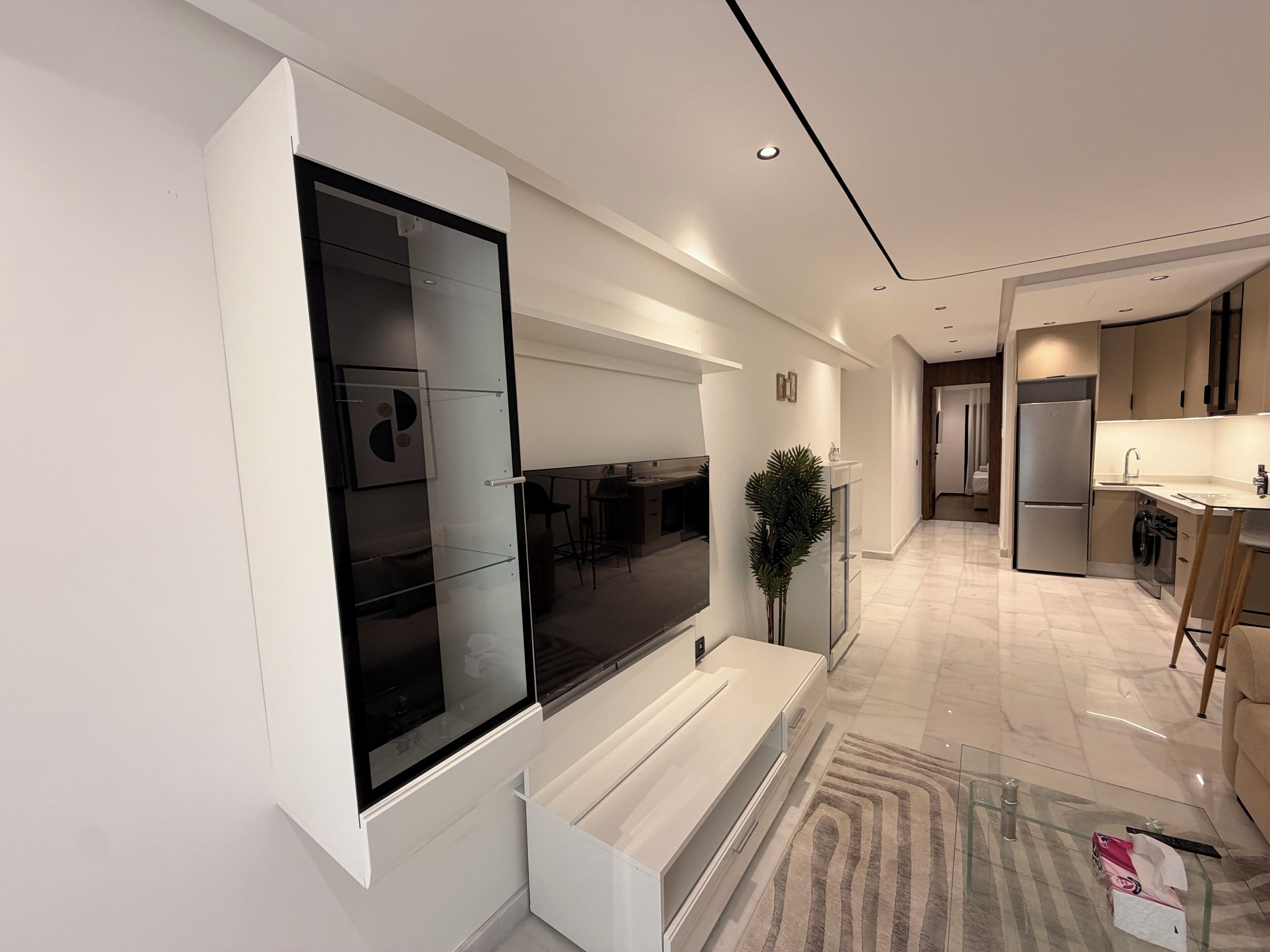 A modern kitchen with a built-in oven, a refrigerator, and a dining area with a glass table.