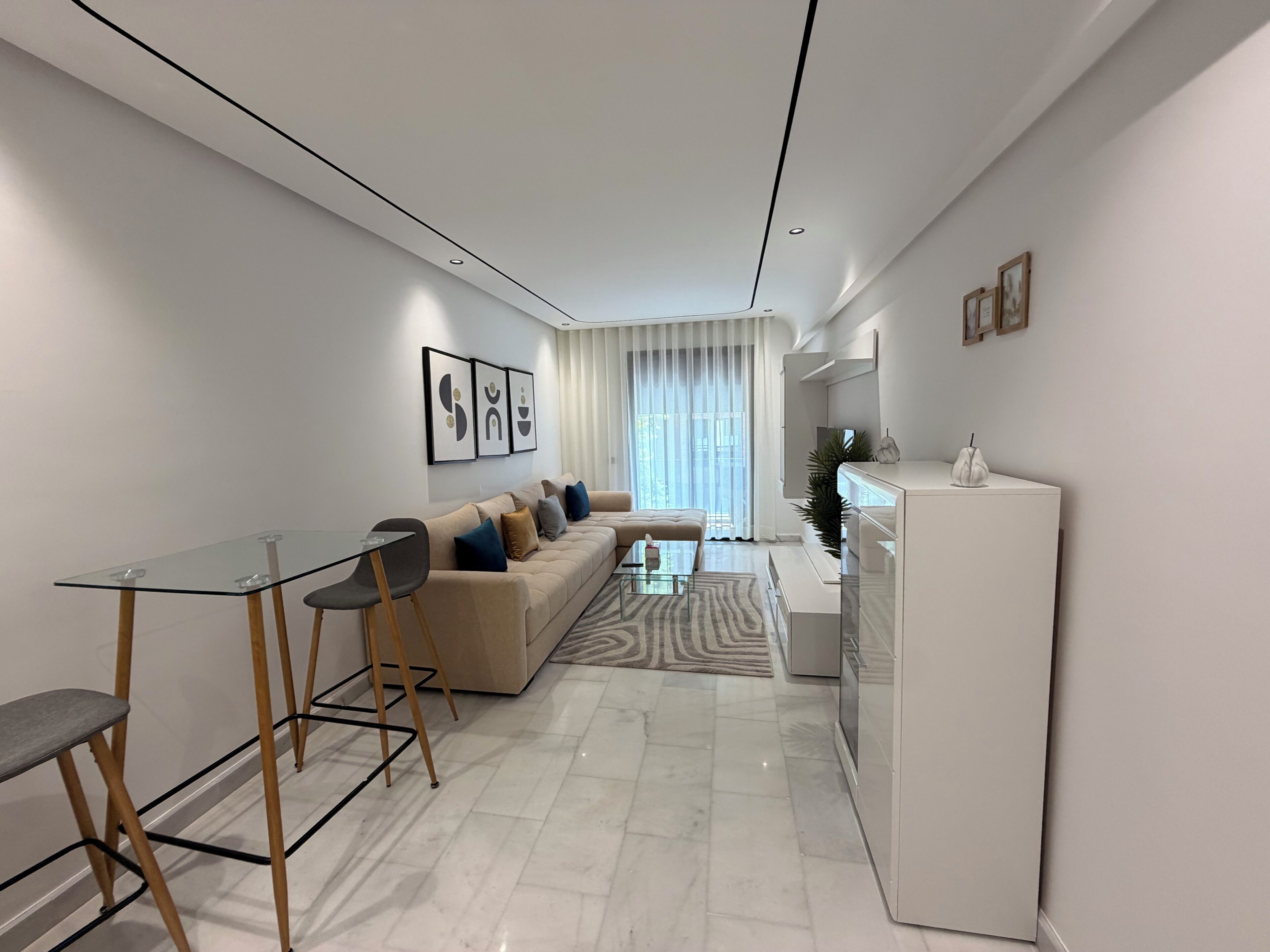 A modern living room with a glass dining table, a sofa, and a white cabinet.