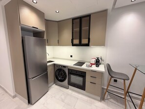 Una cocina compacta con un refrigerador de acero inoxidable, una lavadora y un horno empotrado.
