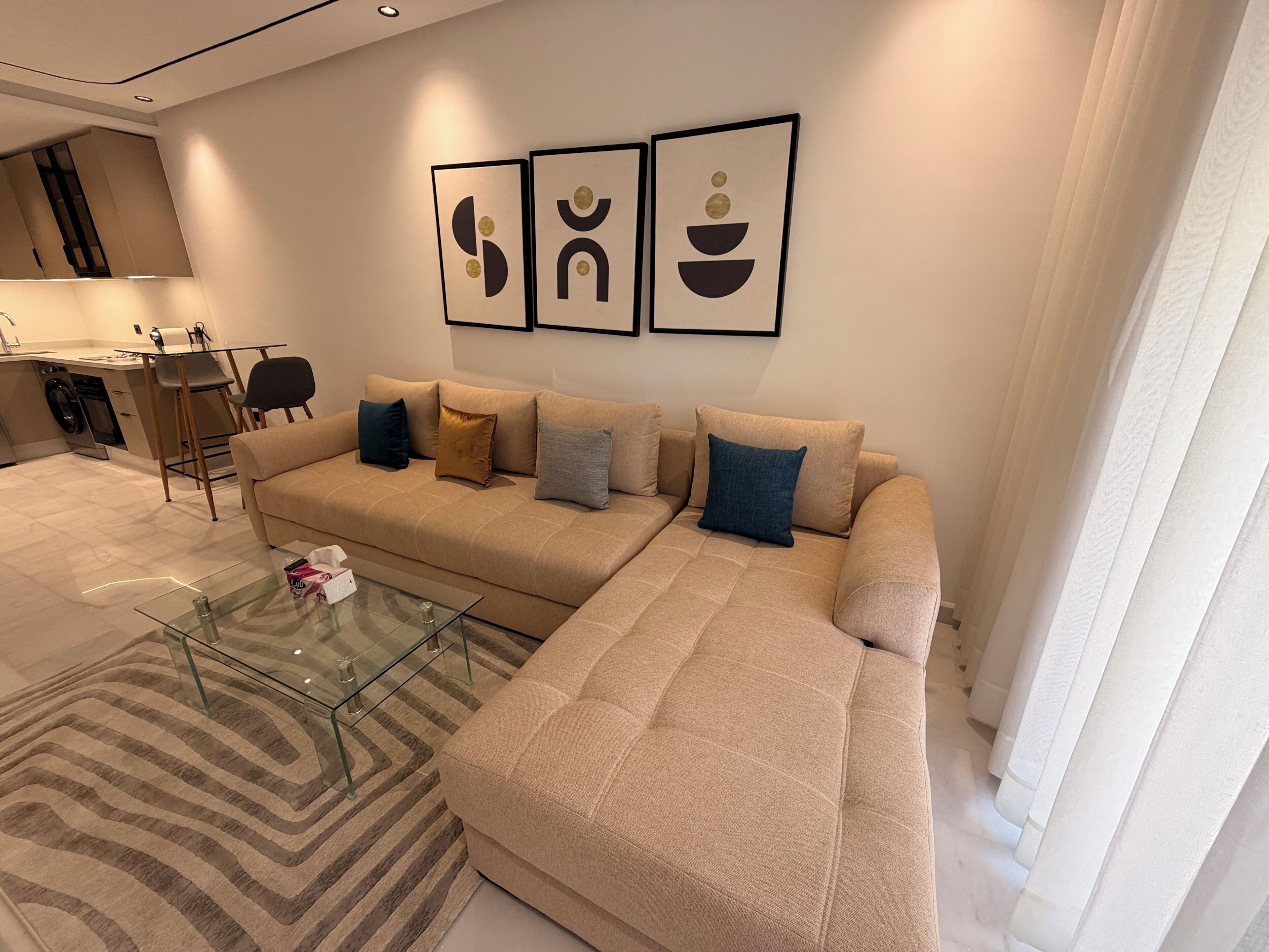 A modern living room with a beige sectional sofa, a glass coffee table, and abstract wall art.