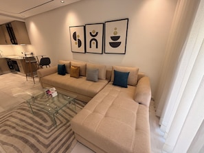 Una sala de estar moderna con un sofá seccional color beige, una mesa de centro de vidrio y arte abstracto en la pared.