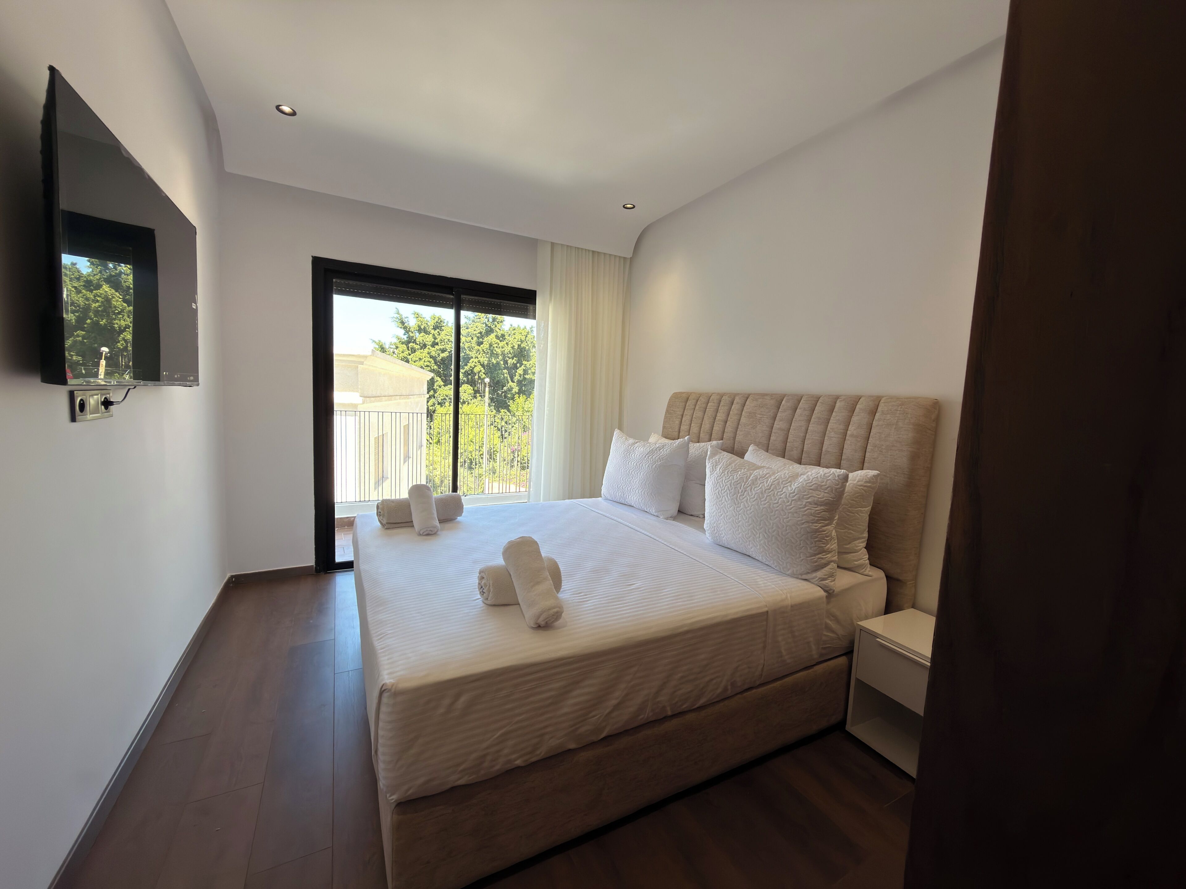 Una habitación de hotel moderna con una cama grande, un televisor de pantalla plana en la pared y un balcón con vistas a zonas verdes.