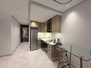 A modern kitchen with a built-in refrigerator, a sink, and a glass dining table. - Golden Maarif Palmiers Apartment (Casablanca)