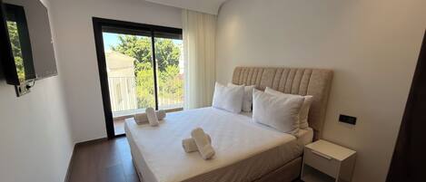 A modern bedroom with a large bed, a nightstand, a flat-screen TV, and a sliding glass door to a balcony.