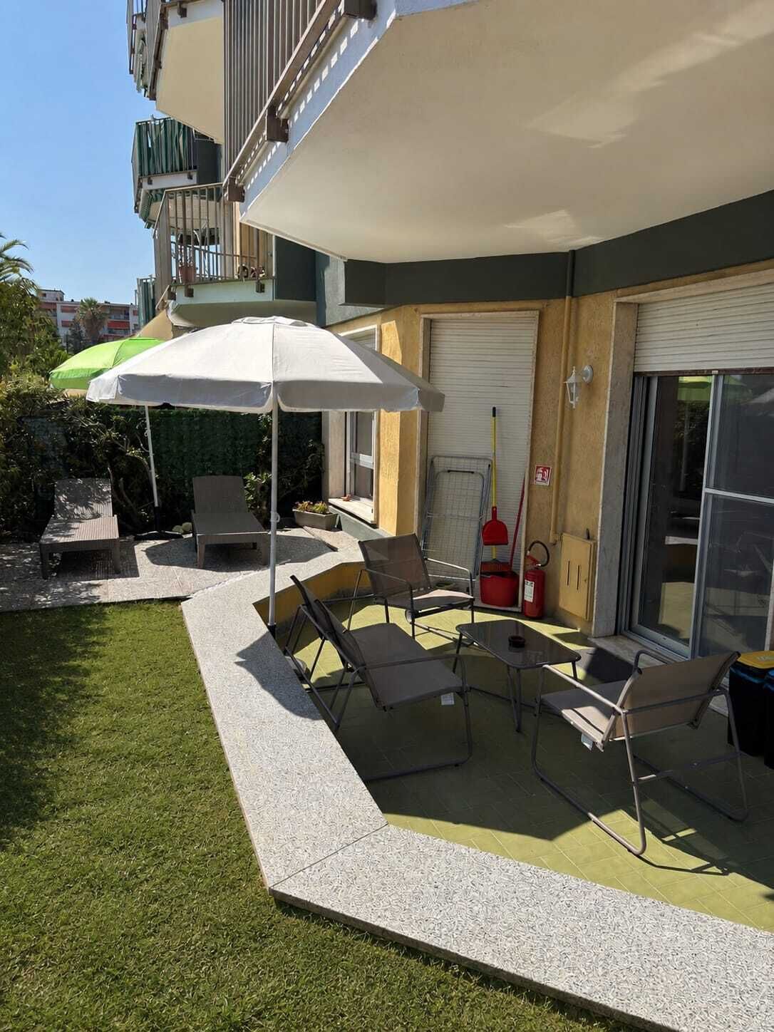 Una zona patio con mobili da esterno, un ombrellone bianco e un estintore.